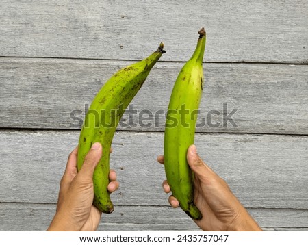 photo holding two green plantains. wooden background Royalty-Free Stock Photo #2435757047