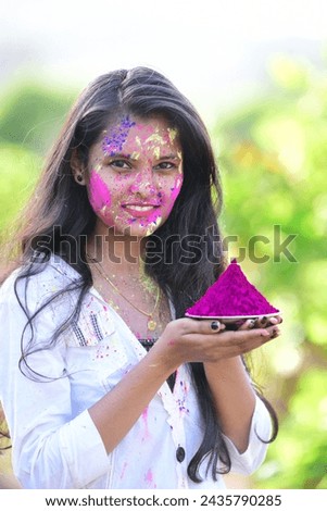 Beautiful Indian girl applying colours on her face, holding colour thali. Celebrating Holi Festival. Royalty-Free Stock Photo #2435790285