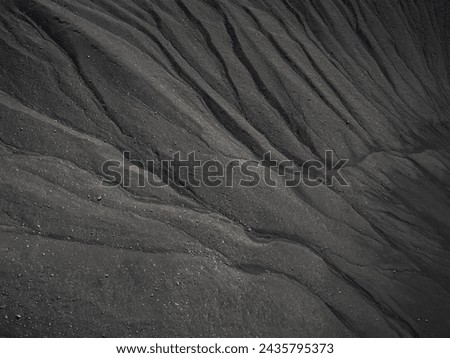 Dark sand as a background, black volcanic sand waves texture, aerial close up shot. Nature pattern concept.