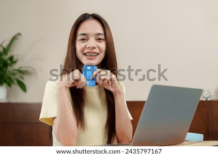 Ecstatic young shopper with dental braces looks at laptop, holding credit card for an online purchase. Exuberant individual with a blue credit card smiles, anticipating an online buy, laptop open