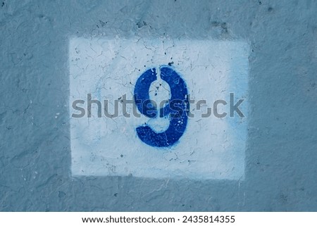 Number nine drawn on a scratched blue wall in a white rectangle