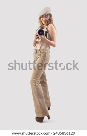 Smiling girl holding an old-fashioned retro camera, dressed in vintage style. Photo service or influencer content creator for social media. Second hand store concept. Isolated on background
