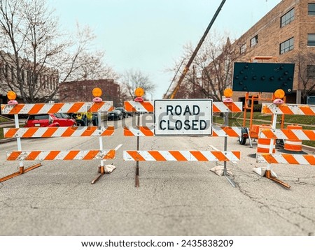 Road Closed Sign and Barricades on a City Street. Orange and white barricades with flashing lights block the street. City buildings in background of view.