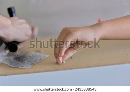 A child actively participates, observes, and learns alongside an adult while assembling new furniture in their home. Symbolizes the transfer of experience to the younger generation and the shared work