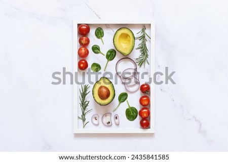 Bright composition with salad ingredients such as avocado, baby spinach leaves, onion, tomatoes, rosemary and spices on wite marble background with white picture frame. healthy food concept.