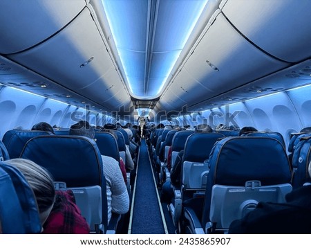 An airplane cabin with beautiful lighting and passengers sitting with their backs towards the camera Royalty-Free Stock Photo #2435865907