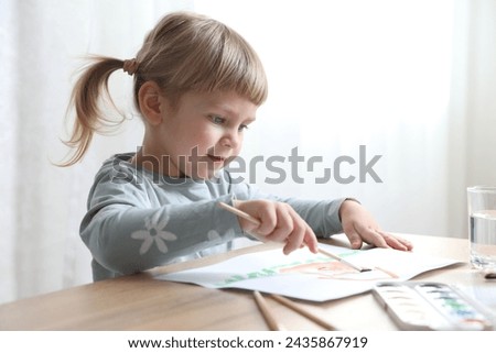 Cute little girl drawing with brush at wooden table indoors. Child`s art