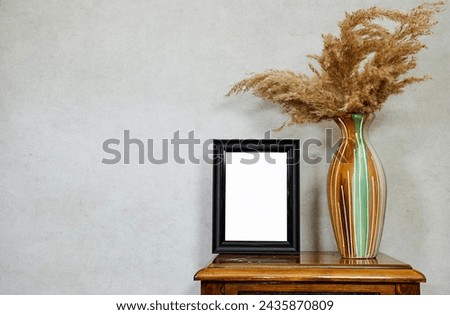 empty picture frame mockup and golden reeds plant vase on wooden table near grunge wall, autumn fall concept
