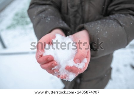 A little child holding the snow in the hands in winter time. Romantic background.
