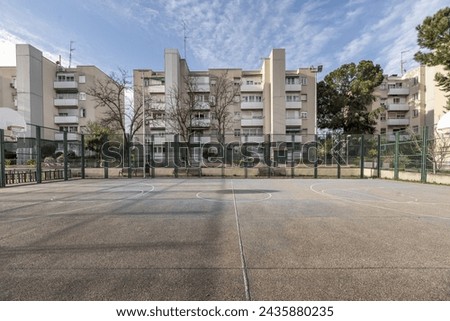 An urban basketball court with rough cement floors with metal fences surrounded by residential buildings