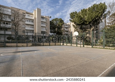 An urban basketball court with metal fences surrounded by residential residential buildings