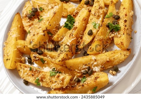 greek lemon potatoes with garlic, parmesan cheese, capers and parsley on plate on white wooden table, dutch angle view, close-up Royalty-Free Stock Photo #2435885049