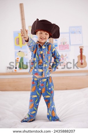 Child, portrait and happy for pirate game, character and creativity in bedroom or at home. An excited boy or kid on a bed with cardboard, cap and pajamas for fun holiday, imagination and play alone