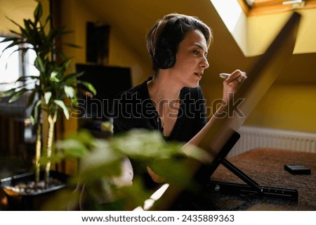 Side view of a creative female illustrator listening music on headphones while pencil drawing on a drawing board at home. Portrait of an inspired female cartoonist sketching a sketch on a paper.