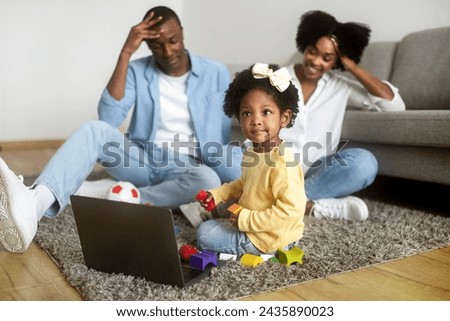 Happy black family watching cartoons on laptop at home. Millennial african american father and mother sitting next to their toddler daughter on floor, looking at computer screen. Family entertainment