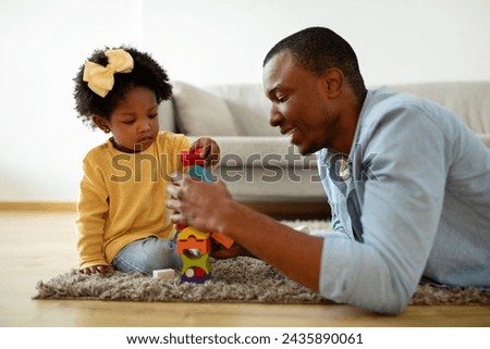 Kids development. Happy young single african american father spending time with his cute little daughter at home, sitting on floor and playing wooden cubes. Fatherhood concept Royalty-Free Stock Photo #2435890061