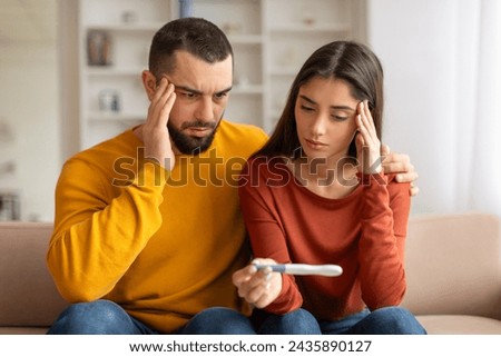 Portrait Of Upset Young Spouses Looking At Negative Pregnancy Test, Suffering Infertility Problems, Depressed Millennial Couple Sitting Together On Couch At Home, Having Health Issues, Closeup Shot
