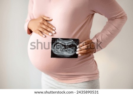 Pregnant woman lovingly showing her ultrasound photo and tenderly embracing belly, expecting mother demonstrating first image of her unborn child, symbolizing the joy and anticipation of pregnancy
