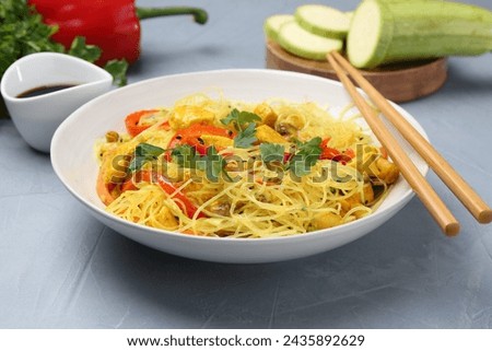 Stir-fry. Delicious cooked noodles with chicken and vegetables in bowl served on gray textured table, closeup