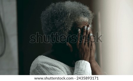 Regretful African American elderly 80s woman covering face with hands feeling anguish and worry about difficult circumstances during old age standing at home residence Royalty-Free Stock Photo #2435893171