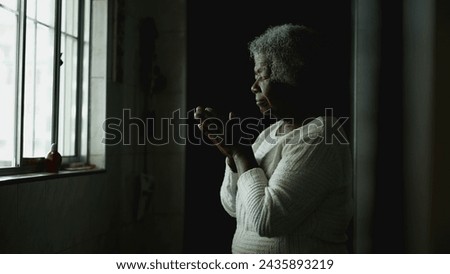 Spiritual African American Elderly Lady in Deep Meditation, hope prayer scene of a black senior woman with gray hair standing by kitchen window with eyes closed Royalty-Free Stock Photo #2435893219