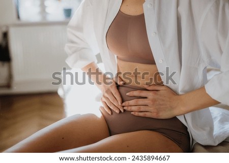 Woman at home suffering from menstrual pain, having cramps. Close up of woman holding abdomen, endometriosis, and conditions causing pain in tummy. Royalty-Free Stock Photo #2435894667