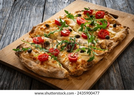 Roman pinsa with mozzarella cheese, capers, arugula and garlic on wooden table  Royalty-Free Stock Photo #2435900477