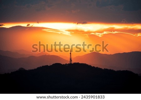 landscape of a sunset in the mountains, images with a lot of contrast and a large orange and reddish sky typical of the golden hour, in the center of the photo you can see a large radio antenna Royalty-Free Stock Photo #2435901833