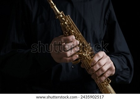 soprano saxophone in hands on a black background Royalty-Free Stock Photo #2435902517