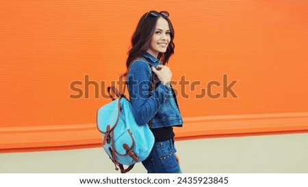 Summer portrait of happy smiling brunette young woman with backpack walking along city street, orange background