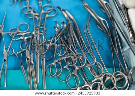 Sterile surgical instruments and tools including scalpels, scissors, forceps and tweezers arranged on a table for a surgery, Sterilized surgical instruments on the blue wrap	 Royalty-Free Stock Photo #2435925933