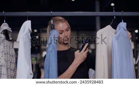 A young blonde woman takes pictures of clothes on a smartphone in store, a shot of a young woman in a store with a smartphone in her hands, woman takes a video or photo for social networks in a store.