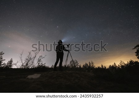 Male landscape astrophotographer with a camera on a tripod outdoors in early spring at night under the starry sky.  Royalty-Free Stock Photo #2435932257