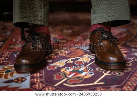 Concept photo of 3-hole boots made of genuine leather worn indoors on a classic red carpet. Close up of Men's legs in stylish brown boots on the Turkish red carpet