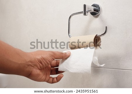 Hand pulling toilet paper roll in holder Royalty-Free Stock Photo #2435951561