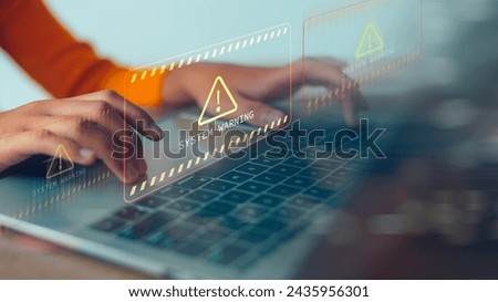 A person is typing on a laptop with a warning sign on the screen. The warning sign is yellow and red, and it is an error message