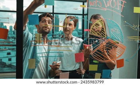Professional business team brainstorm, sharing, thinking idea while skilled male leader write on sticky notes at glass wall. Skilled manager placed business plan on glass wall at office. Tracery Royalty-Free Stock Photo #2435983799