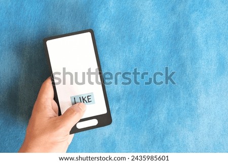 Hand holding a mobile phone paper cutout hitting word like. Social media concept. Royalty-Free Stock Photo #2435985601