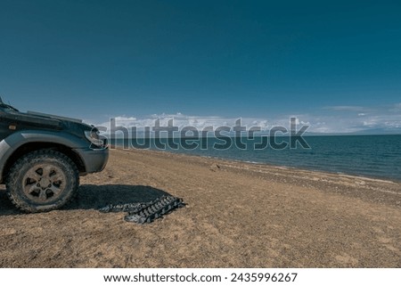 An off-road car with off-road tires on the background of a lake. Sand Track next to the car. Transport for travel.