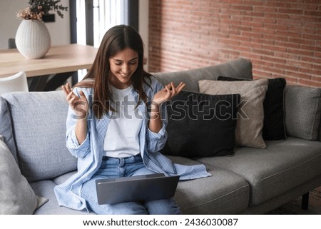 Female sitting on a grey couch using laptop and internet connection and smile. Happy woman in indoor technology leisure activity. Social media life account concept. Adult Lady writing on computer