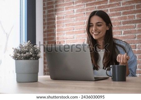 One happy young lady using laptop to videocall friends or business team smiling at the display and gesturing. People and smart working home office workplace lifestyle. Communication with computer Royalty-Free Stock Photo #2436030095