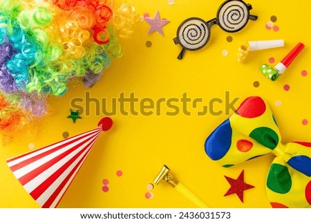April Fool's prank top view setup featuring whimsical glasses, vibrant clown wig, playful bow tie, festive hat, blowers, colorful confetti scattered on sunny yellow backdrop, space for text included Royalty-Free Stock Photo #2436031573