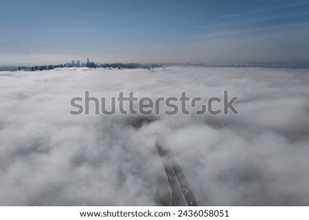 Aerial and morning view of cars driving on the road of Incheon Bridge on sea of clouds against high-rise buildings near Yeonsu-gu, Incheon, South Korea
