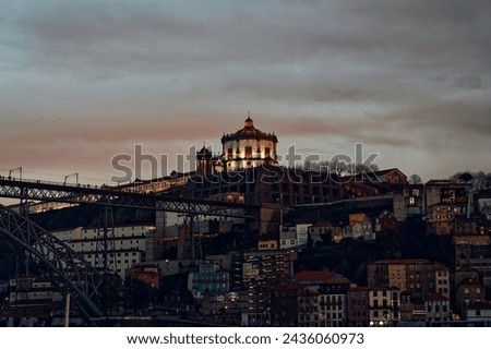 Late afternoon view from the river: serra do pilar monastery looms over porto under a moody sky, its facade aglow, with glimpses of dom luis I bridge and historic buildings beneath.