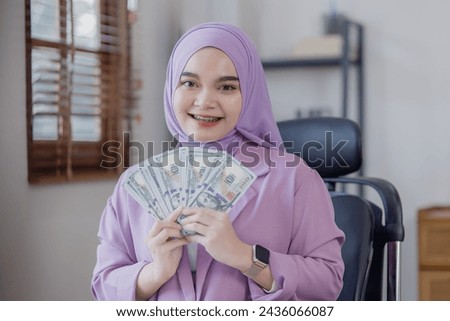 Asian islamic businesswomen holding dollars in hand at office desk.