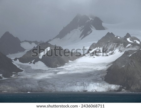  approaching the formidable mountain peaks, icebergs,  and glaciers of elephant island,  on the antarctic peninsula, on a  summer cruise on a  stormy day     Royalty-Free Stock Photo #2436068711