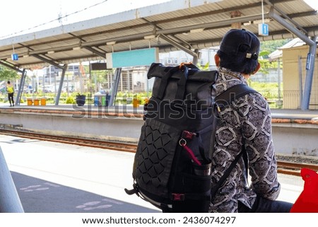 A backpacker is sitting waiting for the train to arrive at the train station