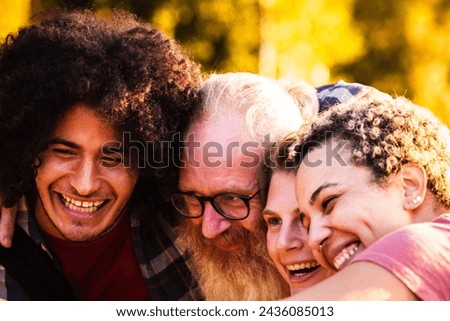 The image captures an up-close, joyful moment among a group of diverse friends. A young man with curly hair is seen laughing alongside an older man with a white beard and glasses, and a young woman Royalty-Free Stock Photo #2436085013
