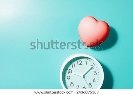 Red heart and white clock on a teal background, depicting love and time concept.