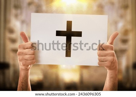 Hands of a religious man with okay sign holding a white poster with drawn cross with church background